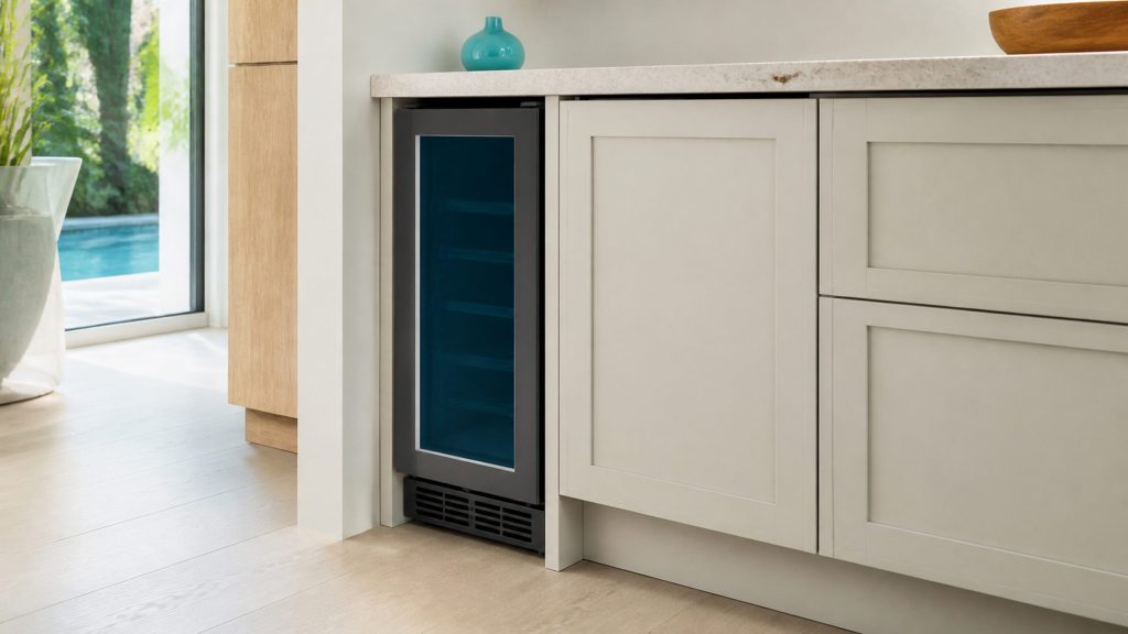 A narrow 15-inch built-under beverage center filling a nook at the end of a pale run, closed, daylight from the side.
