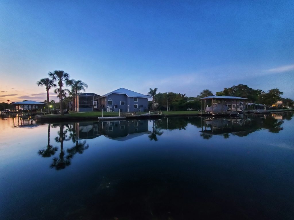 A waterfront house at dusk with palms reflected in the canal